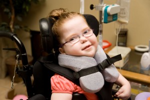 Young girl with cerebral palsy smiles at camera while sitting in her wheelchair at home.