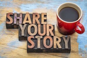 A wooden background with the words "share your story" written in large, block letters. To the right of the text, there is a red coffee cup filled with black coffee.