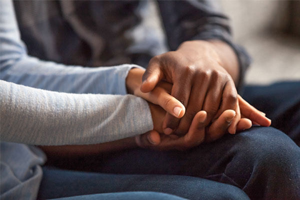 Two people holding hands. One person has a lighter skin tone while the other person has a darker skin tone. The background is blurred, focusing attention on the hands.