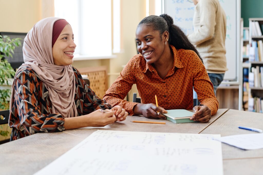 Woman with hijab and black woman seated at table with office supplies