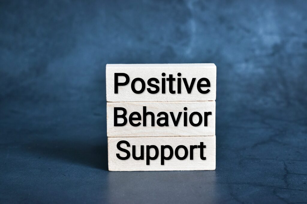 The words "positive behavior support" are written on three separate blocks stacked vertically. The background of the picture is a textured blue surface.