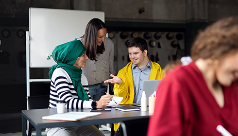 A young male with down syndrome and two women socialize at a desk.