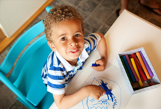 A child drawing with crayons, the perspective is looking from the top down at his face.