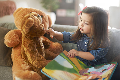 A little girl is reading to her teddy bears.