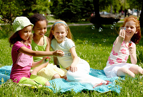 Four girls enjoying time in the park playing with bubbles.