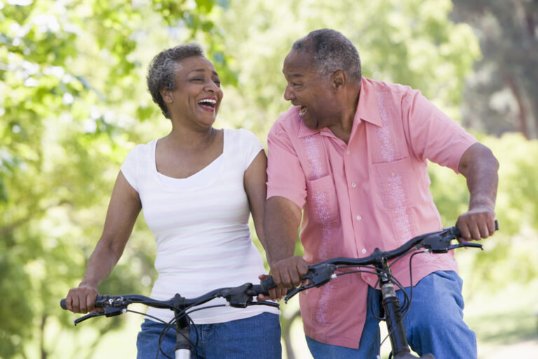 An older couple is riding bikes, smiling and laughing.