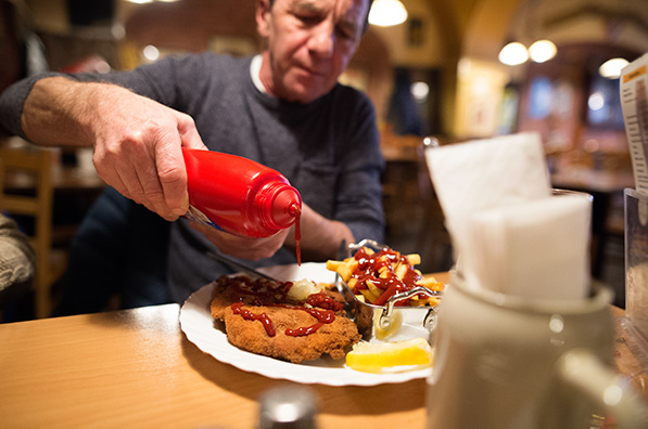 An older man in restaurant puts ketchup on his food.