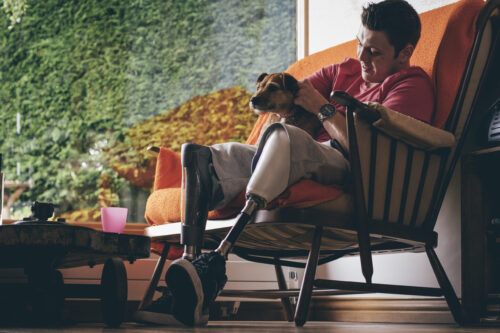 A man sitting in a chair and holding a small dog. The man has two prothetic legs.