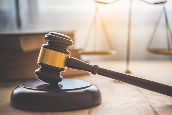 An image of a judge's gavel resting on a sound block. The gavel is made of wood with a metallic band around its head. The background is slightly blurred, but appears to be a courtroom.