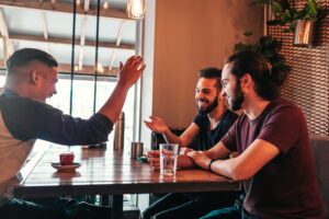 Three men sitting at a table in a restaurant. The men are talking, with one man gesturing with his hand.